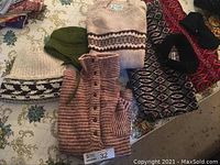 Lot includes multiple wool sweaters and knit hats arranged on a floral tablecloth.