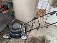 Green and black Yard Works electric lawn mower with foldable handle set up outside shed.