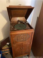Oak Brunswick Victrola cabinet with lid open showing green felt turntable and decorative front grill