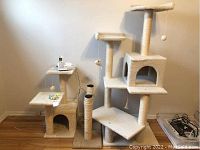 Large cat tower with platforms, cubby hole, scratching posts and toys visible, beige carpeted material