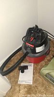 Full view of Craftsman shop vac on carpeted floor with hose connected and attachment laid near base, instruction manual on floor.