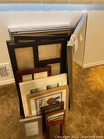 View of 18 assorted picture frames stacked upright against a wall showing various sizes and colors