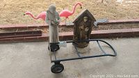 Photo of two concrete St. Francis statues and black hand truck on patio.