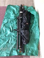 Full view of green tarp with black metal hammock frame parts and black plastic-wrapped hammock fabric on top.