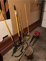 Photo showing a variety of yard tools including rakes, shovels, a broom, saws, an axe, and a gas container.