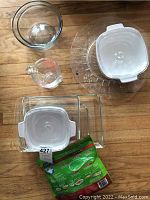 Top-down photo showing 3 Pyrex rectangular glass baking dishes with white plastic lids, one glass measuring cup, and clear glass casserole dishes and platter underneath.