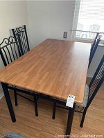 Overall view of rectangular kitchen table with four matching black metal chairs in a room near window