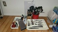 Wide view showing cutlery, knives in wooden block, plastic cutting boards, utensils in red container, and measuring cups in tray