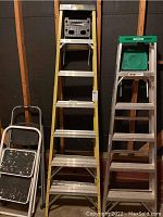 Four ladders: a 7-foot yellow fiberglass step ladder, a 6-foot aluminum ladder with green top, and two small white metal step stools with black rubber treads showing paint wear.