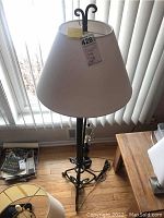 62-inch tall floor lamp with metal scrolling base and white lampshade in front of window