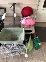 Full view of green spreader, garden fencing panels, red container, pig watering can, green watering can and jerry can, plus gloves and a small plastic item