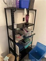 Full view of black metal shelf with three bottom shelves holding various plastic containers and household items; tag attached to shelf side.