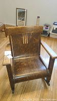 Front view of antique mission oak rocking chair showing the seat, backrest with decorative vertical stripes, and armrests.
