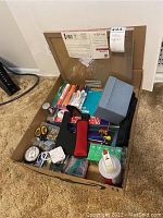 Full box view showing a large assortment of office supplies including notebooks, highlighters, stapler, tape, paper clips and pushpins.