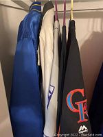 Overall view of five apparel pieces hanging in a closet (Denver Nuggets jacket, Rockies jacket, and three jerseys).