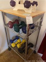 Photo of the chrome rolling kitchen cart with multiple dumbbells placed on shelves, showing the item's structure and condition.