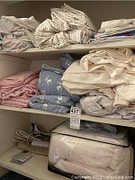 Top shelves of a closet with folded bedding including sheets in multiple colors and patterns, an electric blanket, and a heating pad.