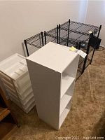 Photo showing the black wire shelving unit behind the white MDF shelving unit and the white plastic storage drawers stacked to the left side.