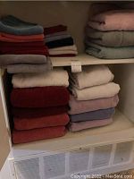 Wide view of linen closet shelves with neatly folded towels in colors including gray, burgundy, white, pink, blue, and taupe.