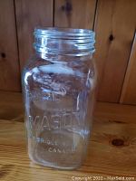 Close-up of a single clear glass mason jar showing embossed 'MASON' lettering and threaded top for lid