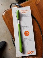 Photo of Slice Precision Cutter in original packaging with green handle, showing product details and branding.