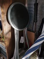 Photo of a brand new stool showing a round black cushioned seat and silver metal legs leaning against a wooden surface with other items in the background.