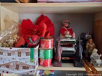 Shelf with red artificial poinsettias, Christmas ribbons, and Christmas figurines including maid and angel figures