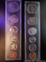 Two vertical clear plastic cases each containing six coins of mixed designs and sizes arranged vertically on dark background.