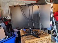 Black LG computer monitor shown upright on a wicker basket with cables draped over the screen and attached to the back. The monitor has its stand connected and the screen is off.