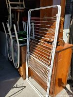 White metal folding drying rack with horizontal bars, set in a room with other household items around.