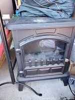 Black freestanding electric fireplace stove with glass front and fake logs inside, showing overall condition and details.
