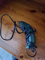 Green electric hot glue gun with power cord coiled around it on wooden surface