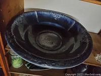 Large dark blue decorative bowl with embossed patterns on outer rim placed on a wooden shelf.