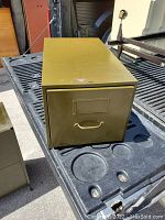 Photo of the metal storage box showing its front drawer with handle and label holder, placed on a truck bed.