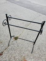 Black metal standing towel rack with two horizontal bars and four legs on a concrete surface.