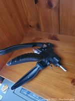 Black handheld hose clamp pliers placed on a wooden surface.