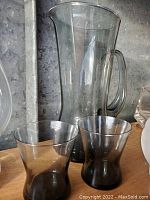 Clear glass pitcher and two tumblers, showing the pitcher in the background and tumblers in front.