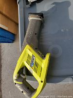 Photo of Ryobi electric reciprocating saw with yellow and gray body and a handle, placed on a gray surface.