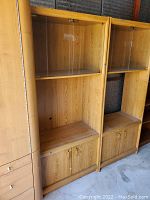 Two tall wooden shelving units with upper shelves, lower shelves, and double-door cabinets at the bottom, placed side by side in a storage area.