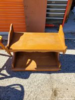 Photo of a wooden side table outside on pavement showing the top surface with raised sides and a lower open shelf.