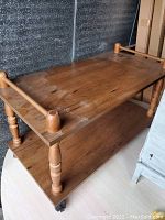 Wooden side table showing top shelf and lower shelf with turned legs on casters.