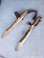 Pair of vintage wooden skate blades with leather straps on concrete floor