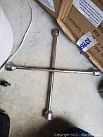 Four-way lug wrench laying on ground, showing cross shape and sockets at each end, with light rust and wear.