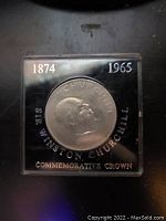 Front view of the commemorative crown coin featuring Sir Winston Churchill, dated 1874-1965, within a protective clear square plastic case.