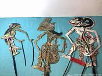 Full view of all 3 Indonesian wayang kulit puppets laid on a blue cloth background, showing intricate details and painted features of Rama, Sita and Ravana figures.