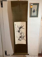 Full view of the bamboo scroll hanging on a white wall next to a framed sailing boat picture.