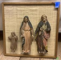 Frontal photo of entire lot showing three carved figures mounted on square framed canvas.