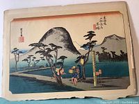 Full image of Hiratsuka: Nawate Road print showing a traditional Japanese landscape with people and pine trees, mounted on paper board with some edge chipping.