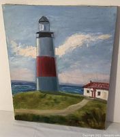 Frontal image of the oil on canvas painting depicting a lighthouse with red band and small white house adjacent on grassy terrain, ocean and sky in background.