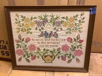 Full view of framed needlework showing floral border, birds, and central text